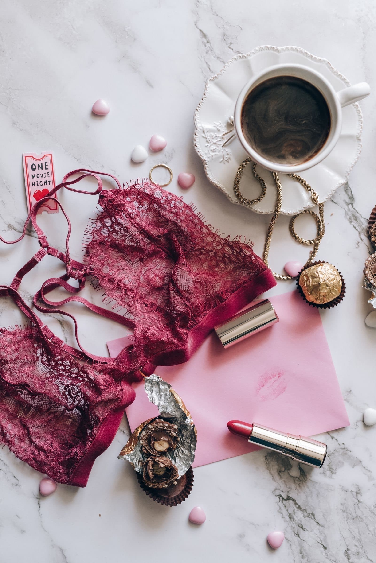 Burgundy lace bralette laid out with morning coffee, chocolates, and a lipstick-kissed note